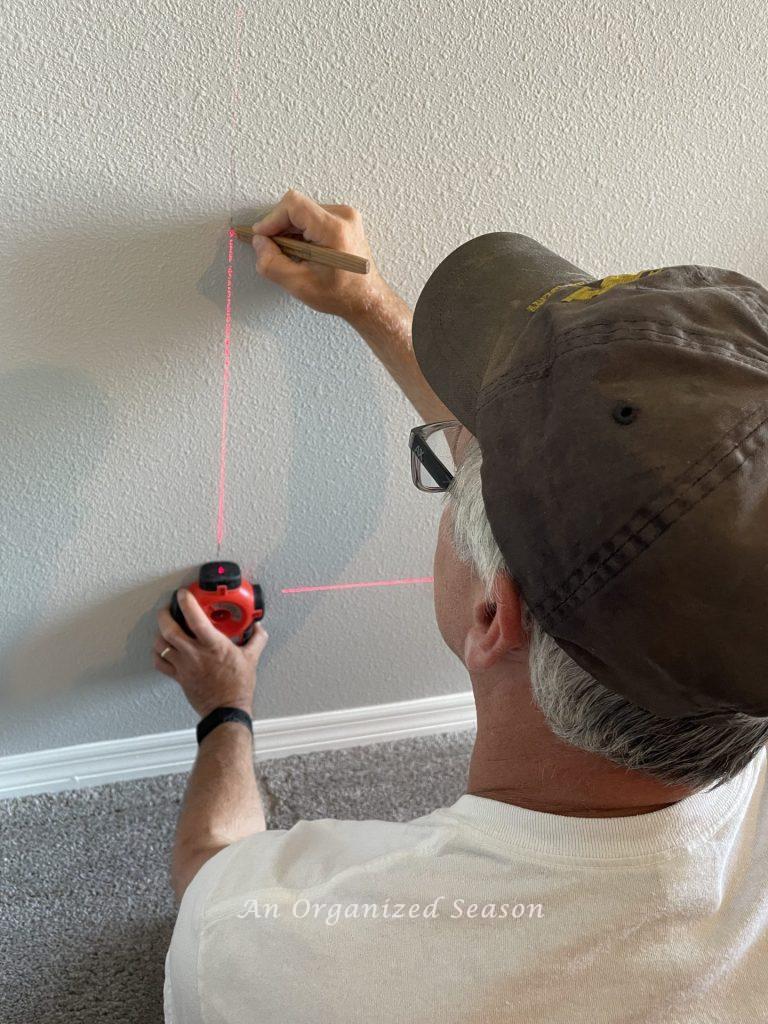 A man using a laser to mark studs on a wall. Step two for advice on installing flooring on  a wall.