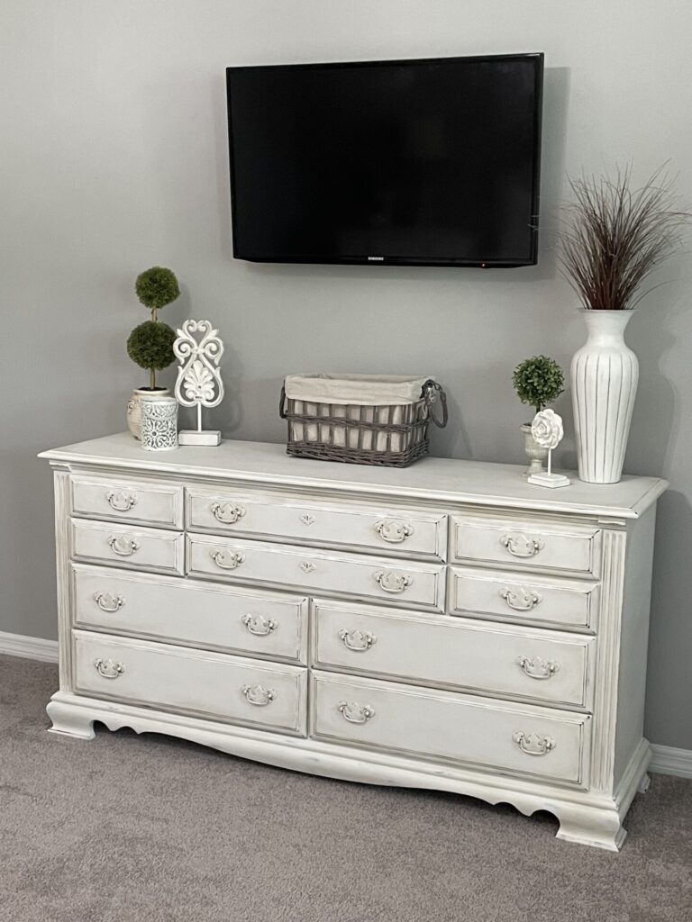 A white painted dresser with TV hanging above it. 