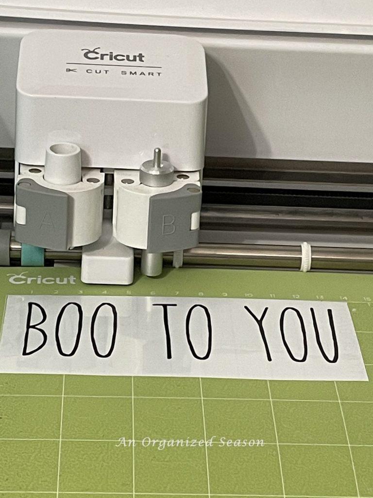 A Cricut machine that cut out the saying "Boo to You" in black vinyl. Step three for how to make a Rae Dunn Inspired candle.