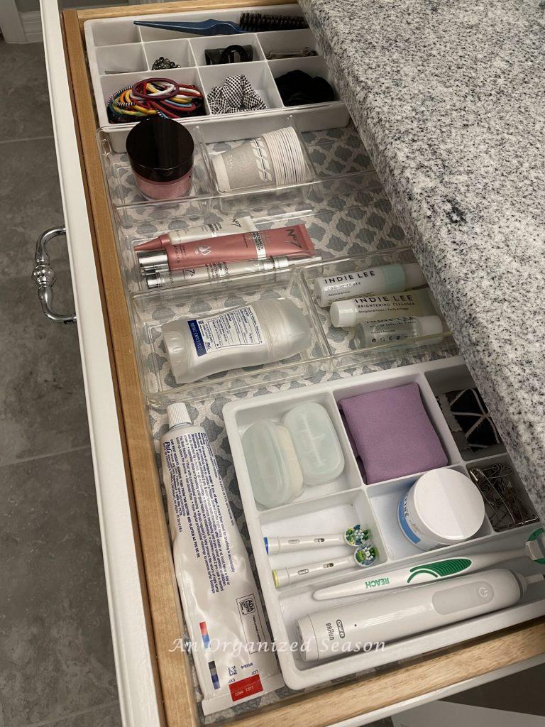 A drawer in a bathroom cabinet with dividers separating hair bands, facial products, and tooth brushing items. An example of master bathroom organization ideas. 