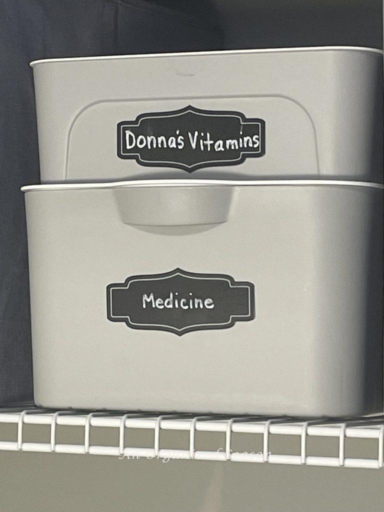 Gray plastic containers with white lids that stack on top of each other. They have black labels for vitamin's and medicine. Example of an organization idea for a master bathroom.