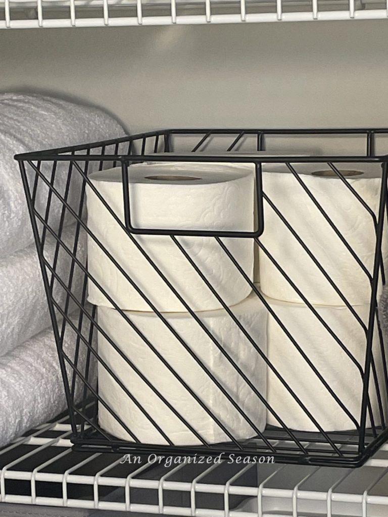 A black wire basket containing several rolls of toilet paper showing a master bathroom organization idea.