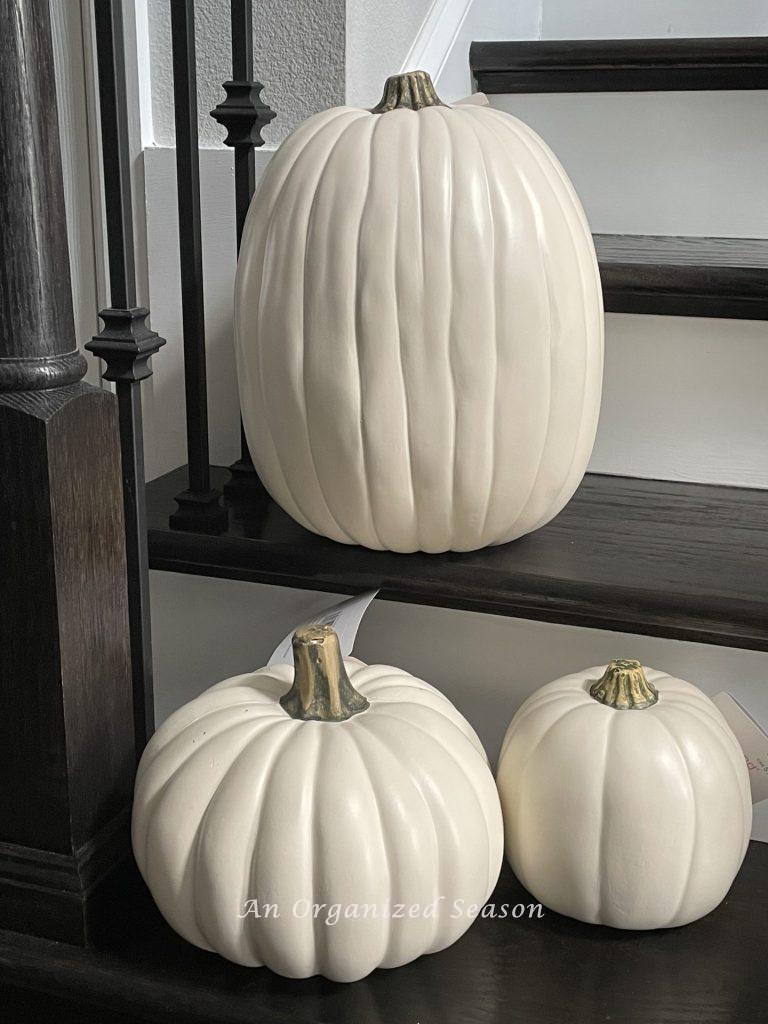 A small, medium, and large and white pumpkins sitting on a staircase. Step one for how to make a pumpkin topiary. 