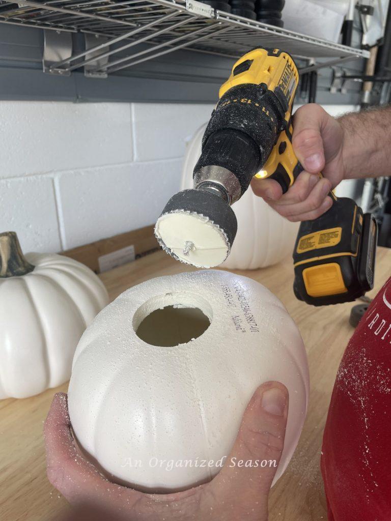 A man drilling a hole in the bottom of a white faux pumpkin. Step two for how to make a pumpkin topiary. 
