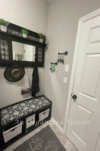 An organized garage entryway decorated with a black bench and mirror holding a hat, purse and jacket.