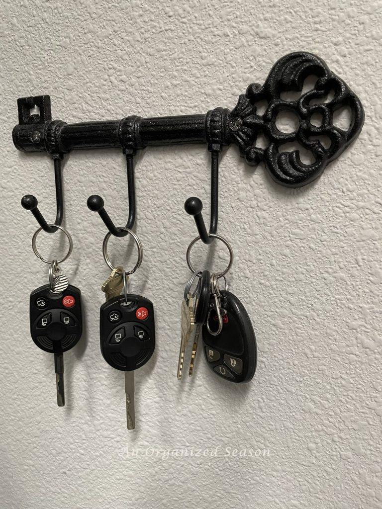 A black metal holder shaped like an old key with three hooks, holding three sets of keys. An example of how to organize every entryway to your home.