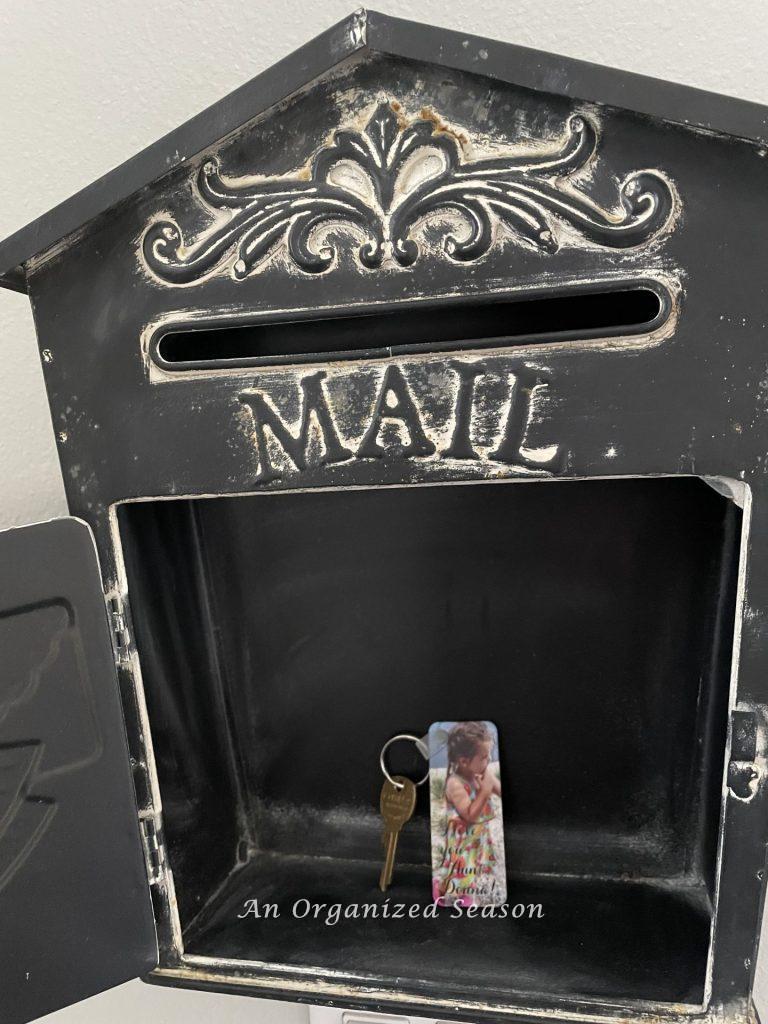 A decorative black metal mailbox hanging on a wall with door open and mailbox key inside. An example of how to organize the entryway to your home.
