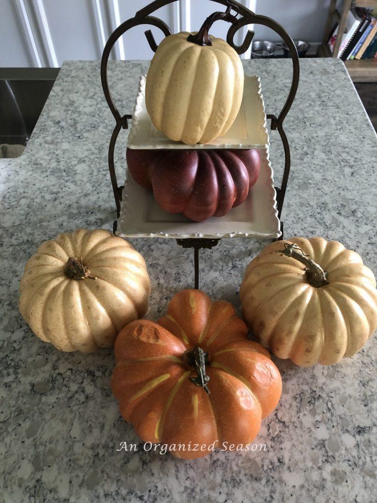 Five faux pumpkins in traditional fall colors on a kitchen counter. Showing before picture of pumpkins that will be painted with pearlescent paint.