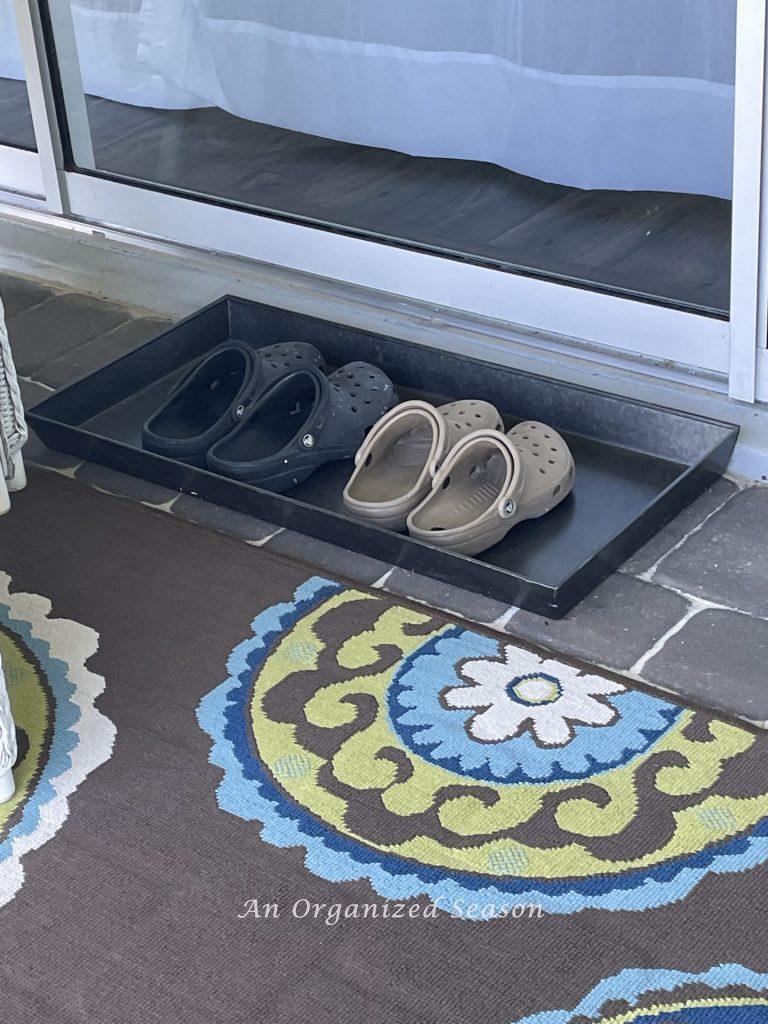 A metal shoe tray placed outside a patio door, with two pair of Crocs shoes sitting inside it. An example of how to organize the entryway to your home. 