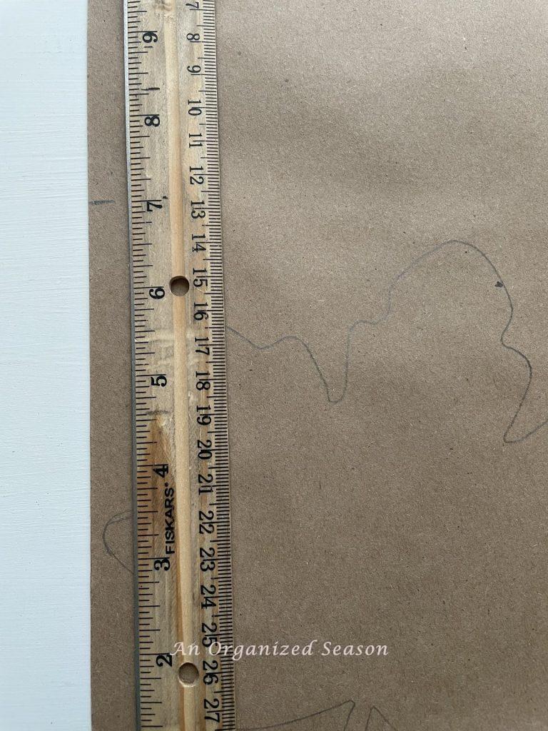 A ruler measuring the length of a traced leaf, showing step two for how to create a simple paper leaf garland.