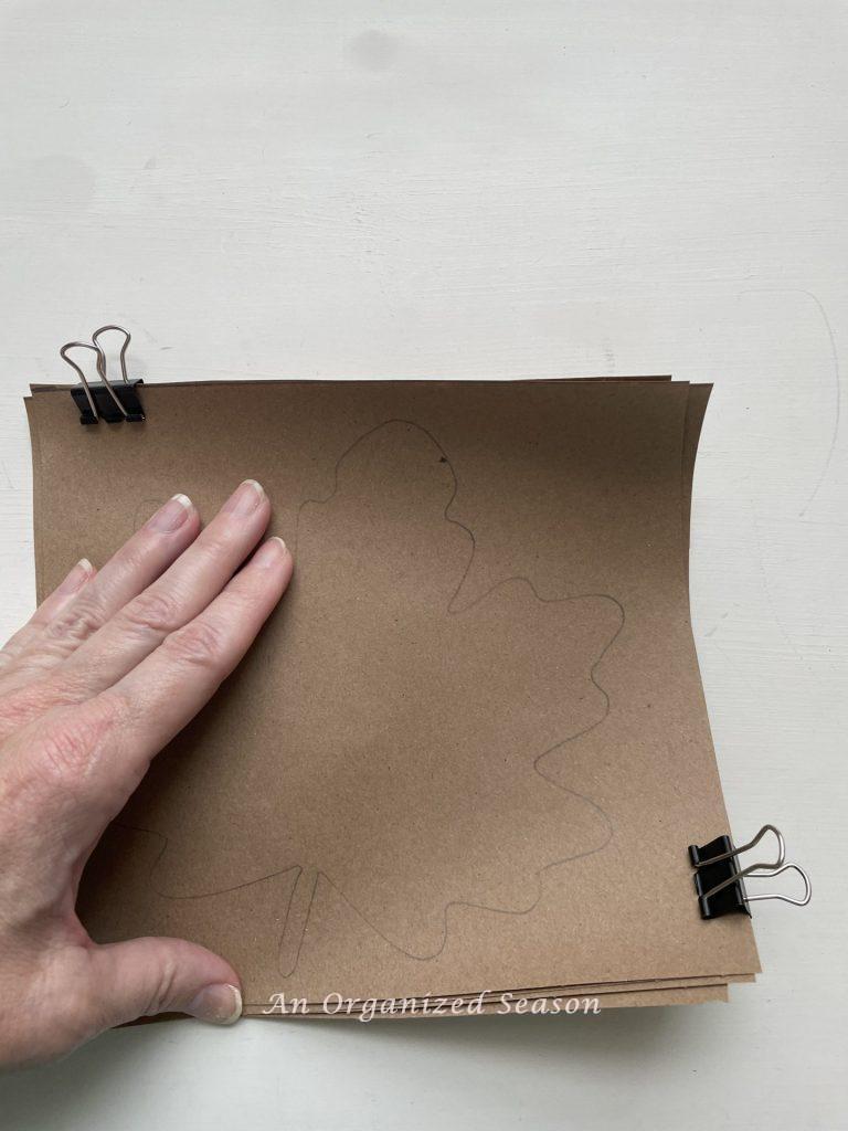 Clip four squares of brown paper together and cut out the leaf shape. Step four for how to create a simple paper leaf garland.