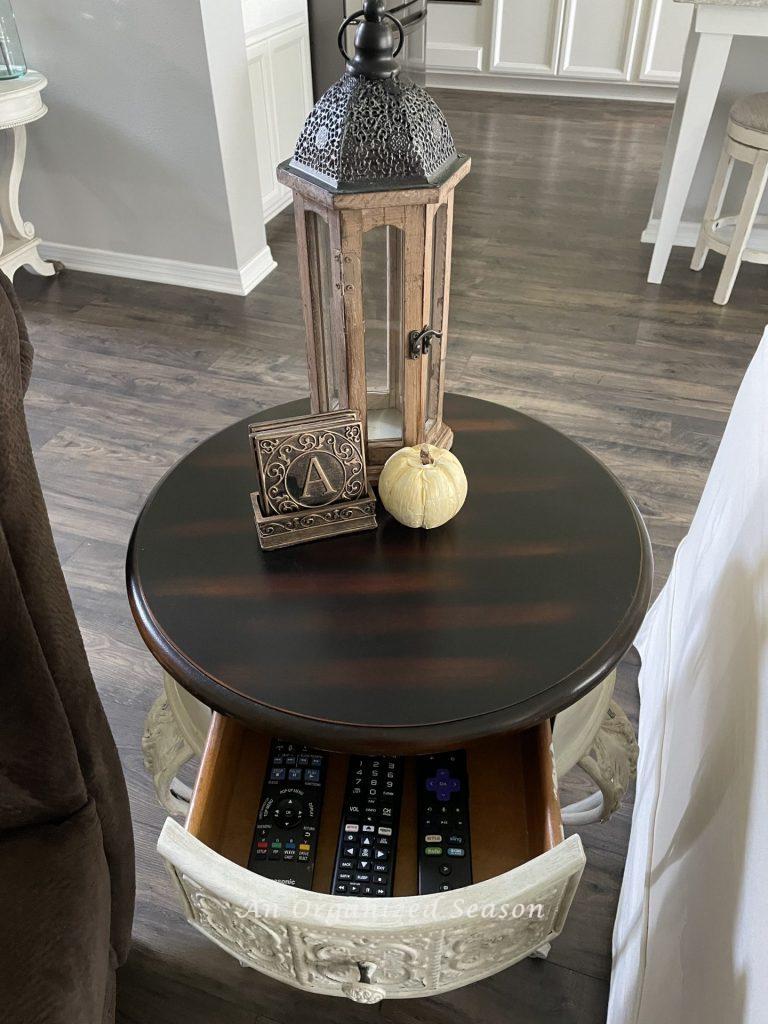 An end table with an open drawer with three TV remote controls stored inside. An example of how to maintain an organized living room. 