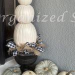 A three-tiered white pumpkin topiary in a black planter surrounded by white and green heirloom pumpkins