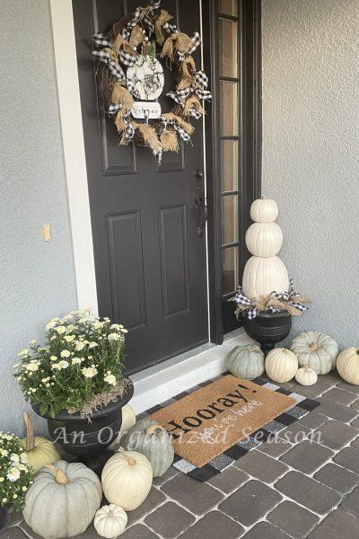 A front porch decorated for Fall with white and green pumpkins, white mums, a buffalo check and burlap wreath and layered doormat!