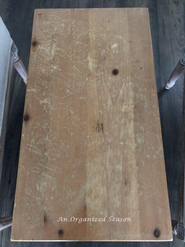 The top of a small wood table that is scratched and stained, ready for a living room table makeover.