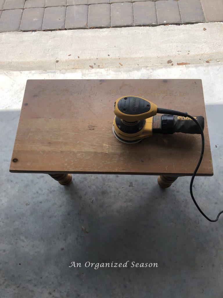 A small wood table with a hand sander sitting on top of it, step one for my living room table makeover.