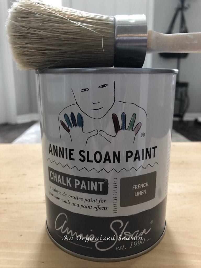 A can of Annie Sloan chalk paint in French Linen with a paintbrush sitting on top. Step two of my living room table makeover.