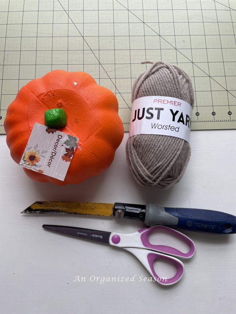 A faux pumpkin, yarn, scissors, craft knife, and ruler. Items needed to make yarn pumpkins.