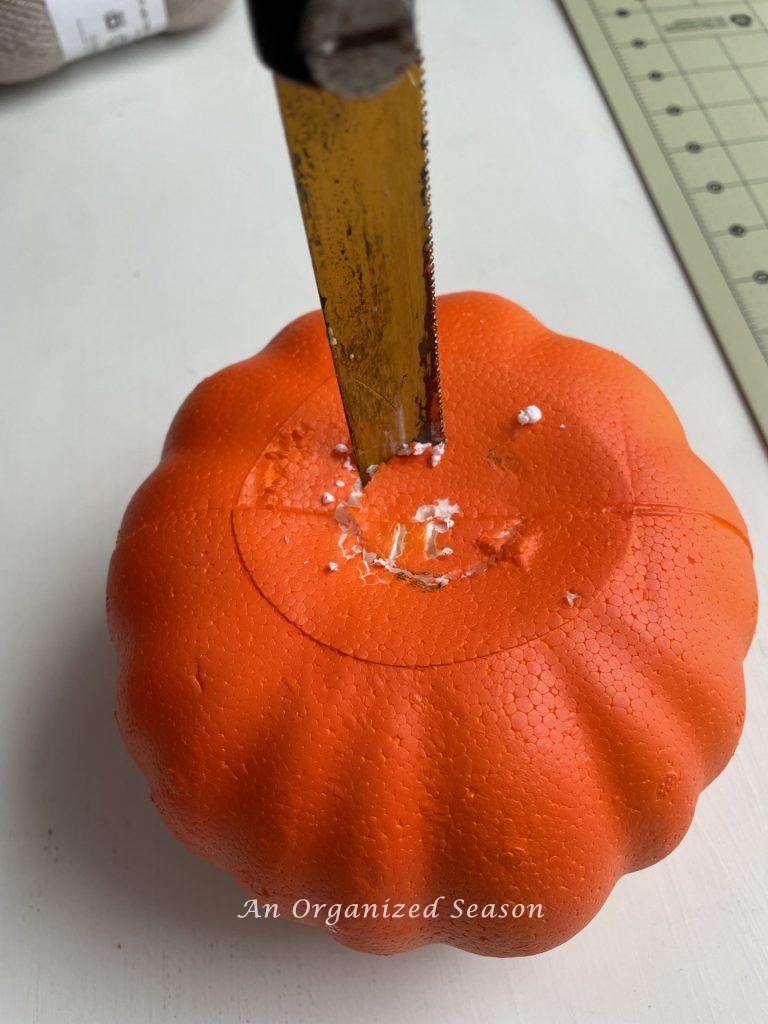 A knife cutting a hole in the top of a styrofoam pumpkin. Step one for how to make adorable yarn pumpkins.
