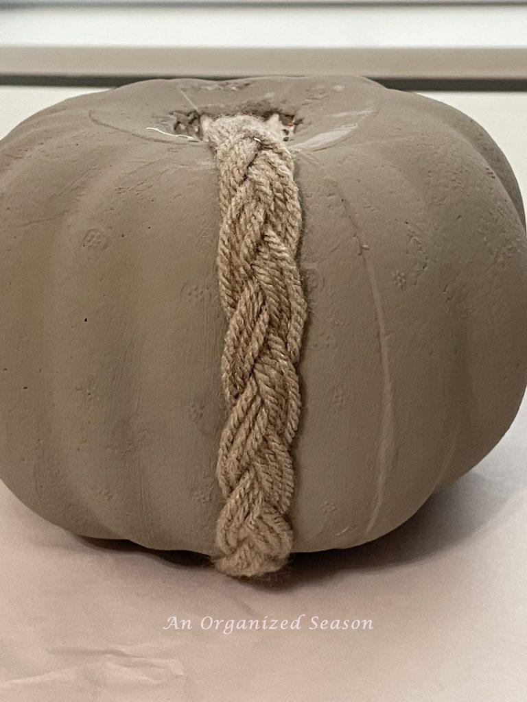 A braided strand of tan yarn that has been glued onto a faux pumpkin. Showing how to make an adorable yarn pumpkin. 