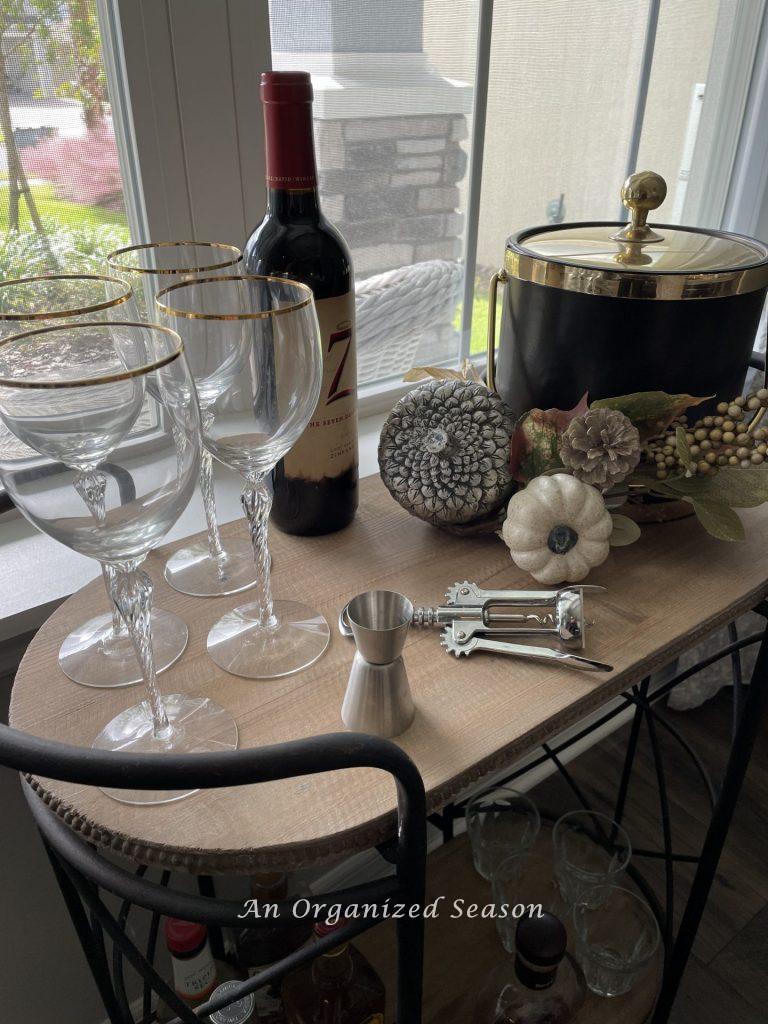 A bar cart in a dining room with wine glasses, wine, a bottle opener, and ice bucket organized in a dining room for easy entertainment.