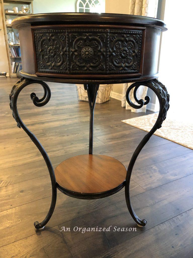 A brown end table that needs to be painted white to match the other living room furniture.