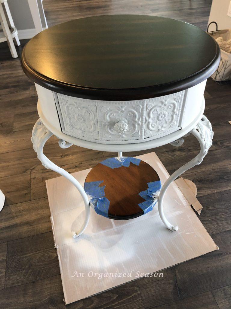 A brown end table that has been painted white (except the top and lower shelf that were left brown) so that it matches the other living room furniture. 