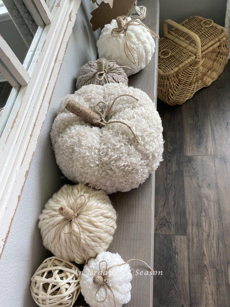 Neutral colored yarn pumpkins with twine stems, sitting on a shelf showing decor inside the best of Autumn home tour.
