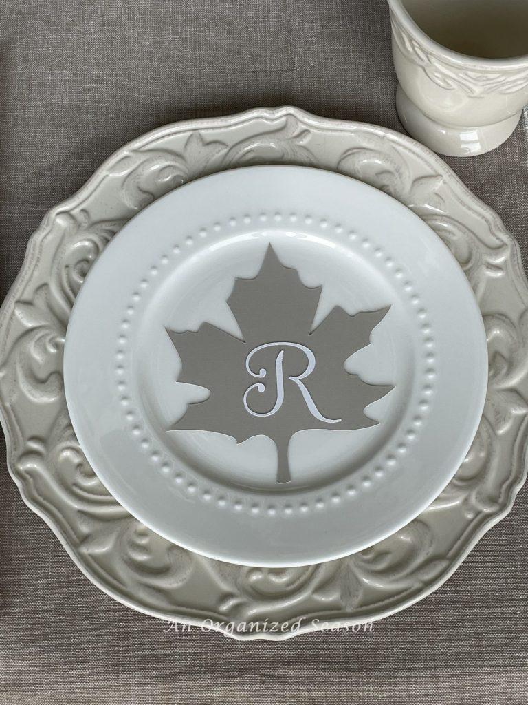 A place setting with cream dinner plate, white salad plate, and a tan leaf with a white letter "R" as a place card. Pretty decor for the best of Autumn home tour.