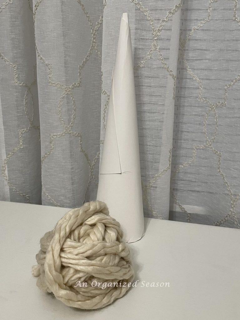 A white poster board cone next to a ball of chunky yarn.