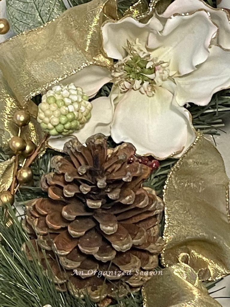 Close up picture of a Christmas wreath decorated with white magnolia blooms, pinecones, and gold ribbon.
