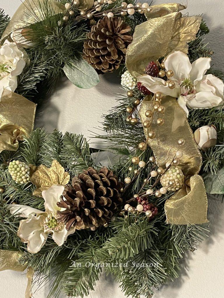 Christmas wreath with white flowers, gold ribbon and pine cones. 