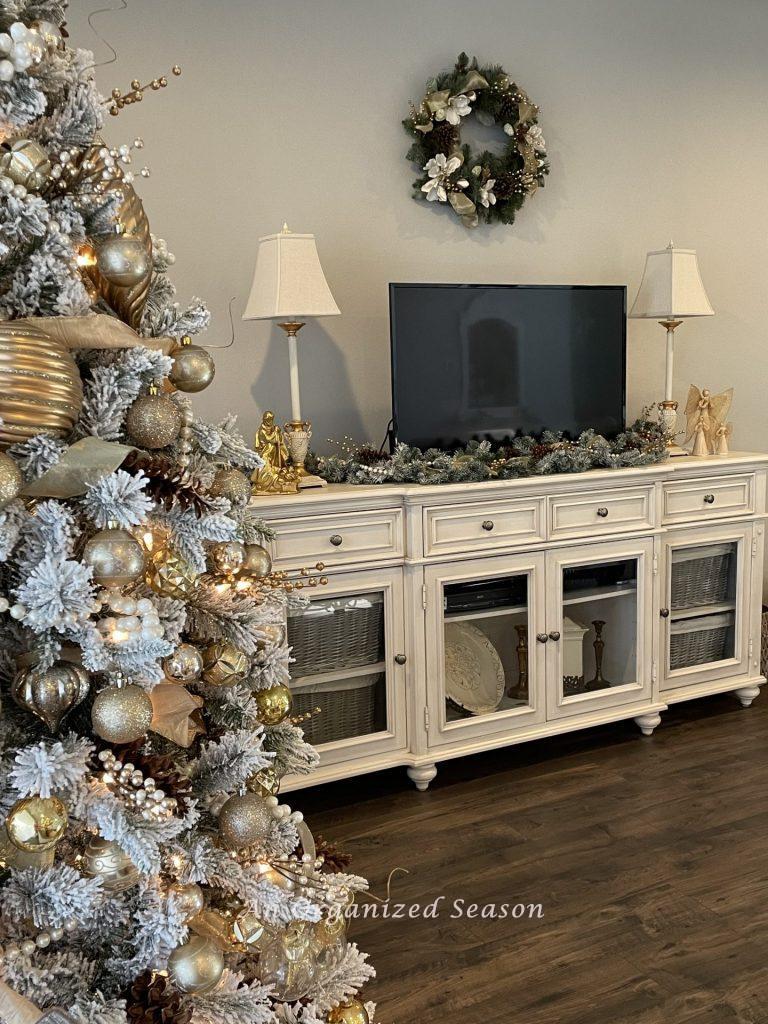Living room TV console table decorated for Christmas with greenery and a wreath above it. 