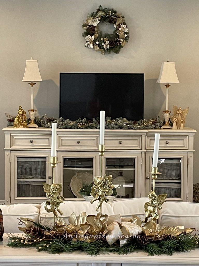 A living room decorated for Christmas with a wreath, garland, and gold angel candle sticks. 