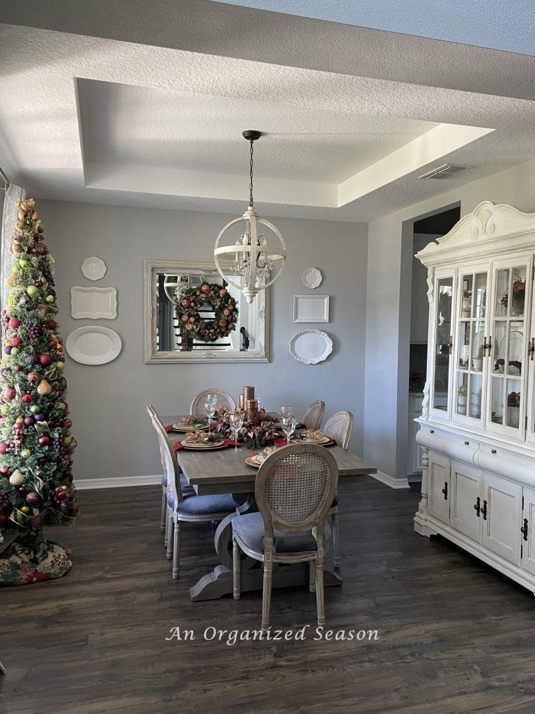 A dining room decorated for Christmas with a skinny tree, wreath, and table setting.
