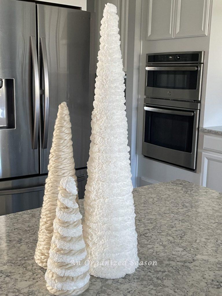 Three yarn cone Christmas trees sitting on a kitchen counter.