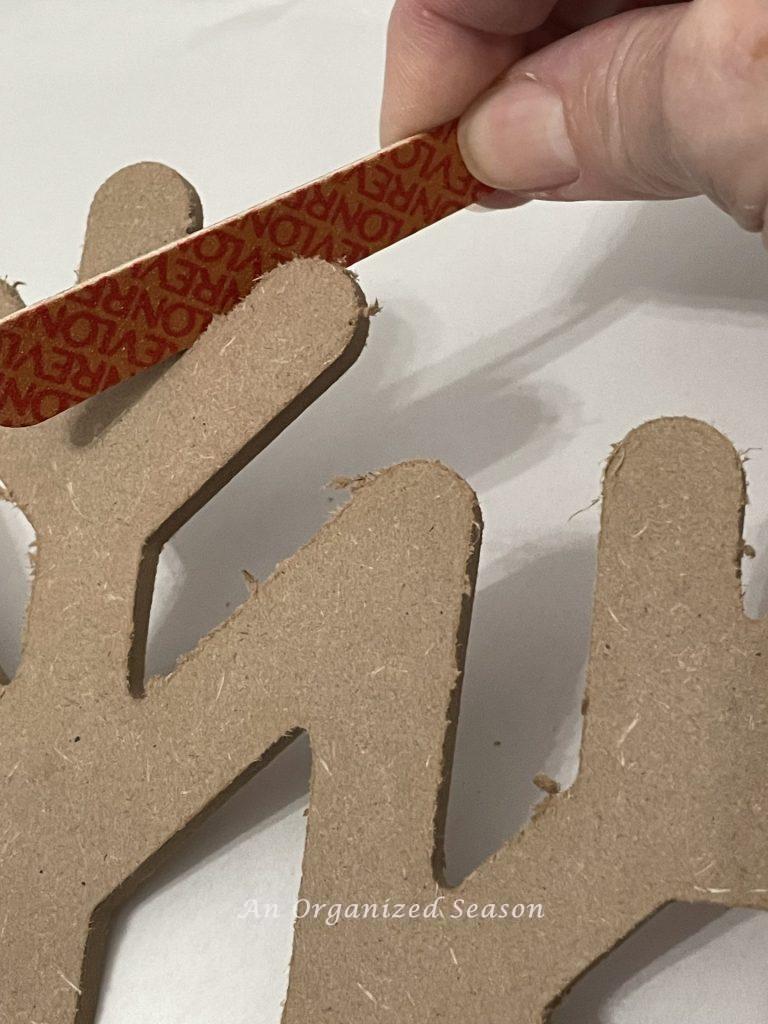 Someone using a fingernail file to remove the rough edges of a snowflake, Step two for how to make a cheap but cute tree topper.