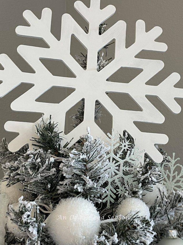 A painted white snowflake sitting atop a tree. The finished product for how to make a cheap but cute tree topper. 