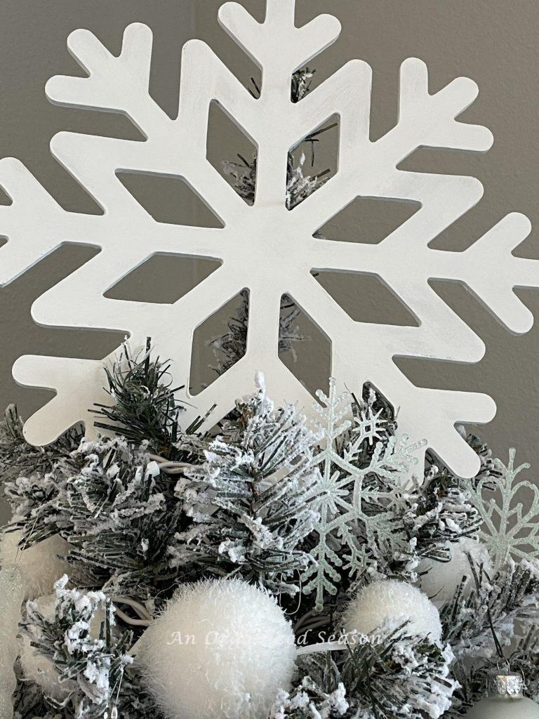 A painted white snowflake sitting atop a tree. The finished product for how to make a cheap but cute tree topper.