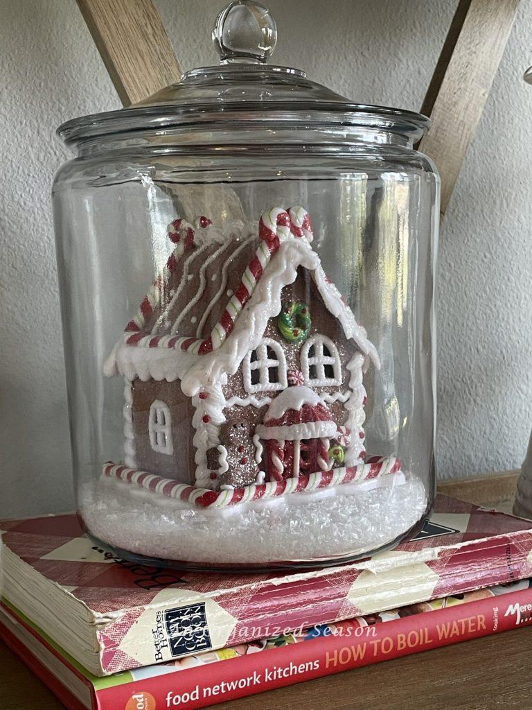 A ginger bread house inside a clear cookie jar sitting on two cookbooks adds a little bit of Christmas to the kitchen. 