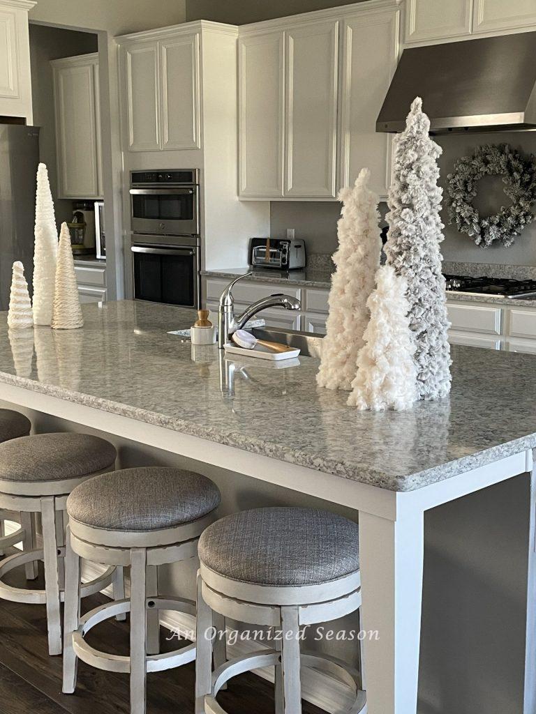 A kitchen island that has six yarn cone trees sitting on it to add a little bit of Christmas to the kitchen.