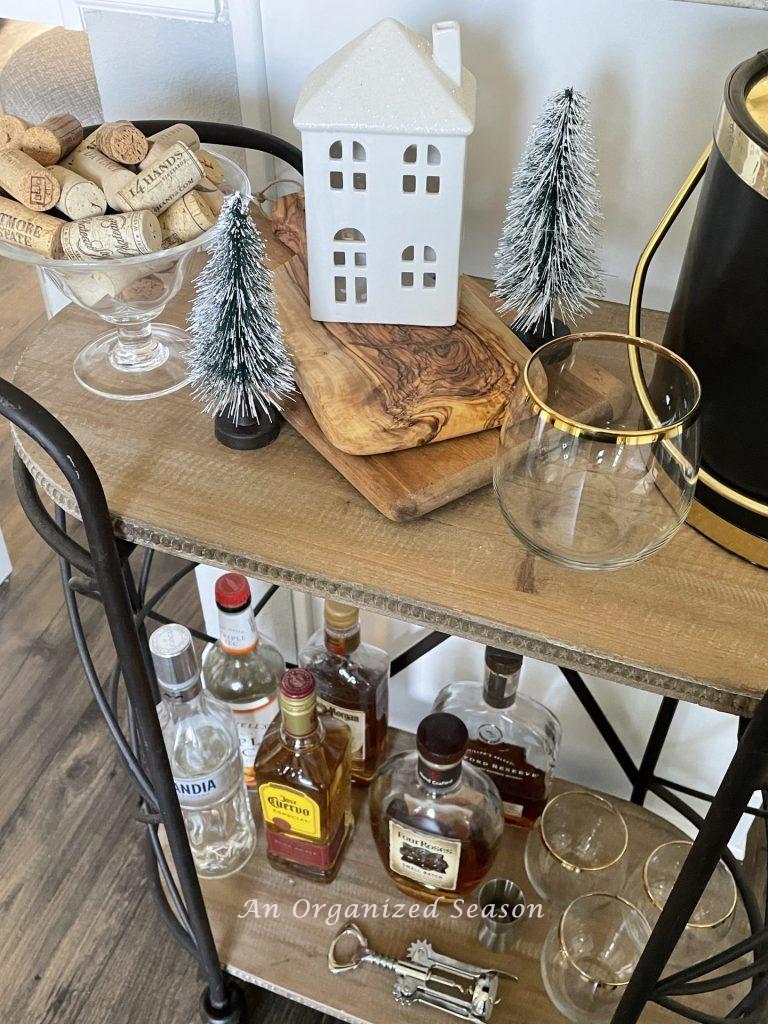 A bar cart with a small white ceramic house, and two bottle brush trees that add a little bit of Christmas to the kitchen.