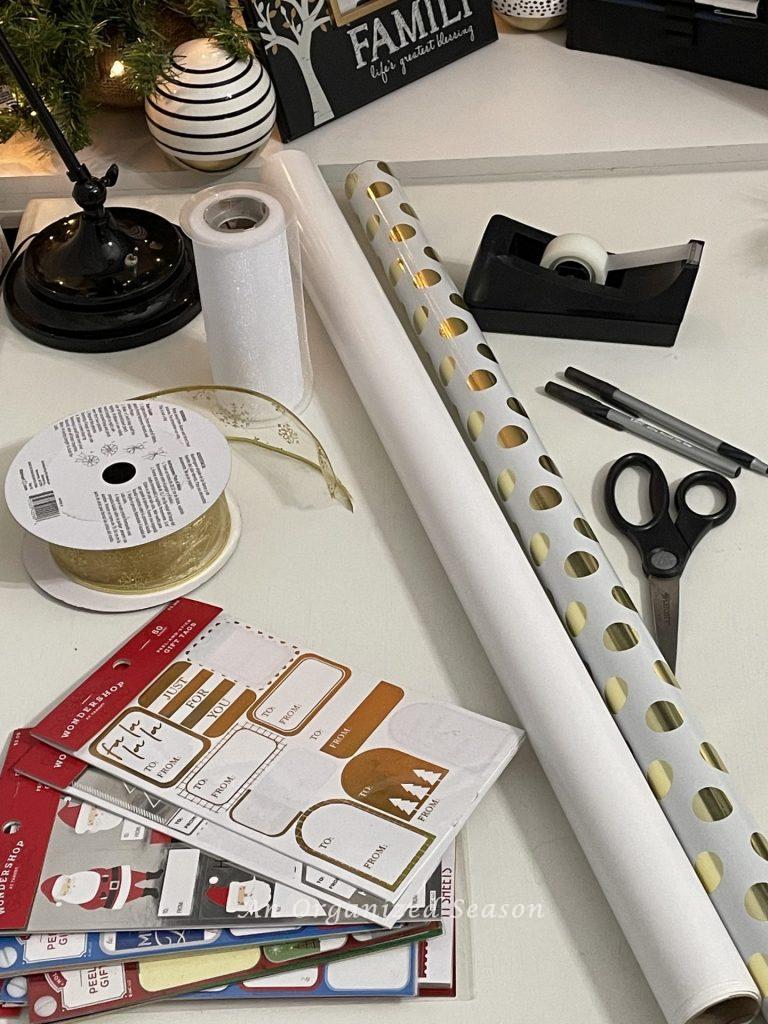 Wrapping paper, ribbon, tags, scissors, tape, and pens sitting on a gift wrapping station.