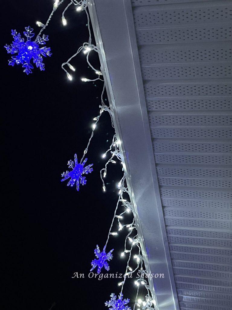 Icicle lights mingled with blue stars hanging from a gutter during the Tis the Season nighttime home tour.