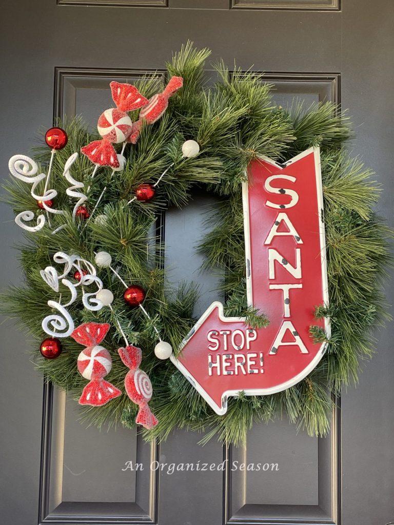 A wreath with a sign saying "Santa stops here" and red and white candy. An example of how to welcome guests with holiday porch decor.