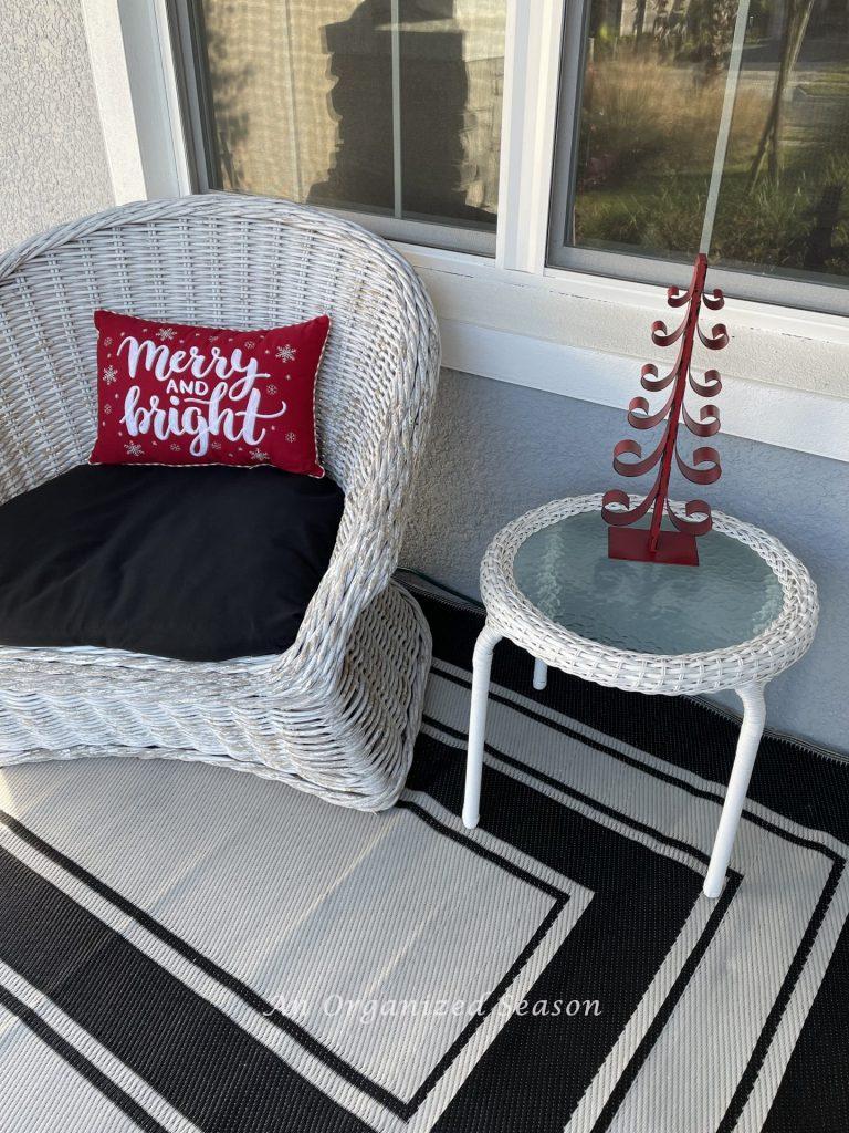 A Christmas pillow and red metal tree add to the holiday porch decor. 