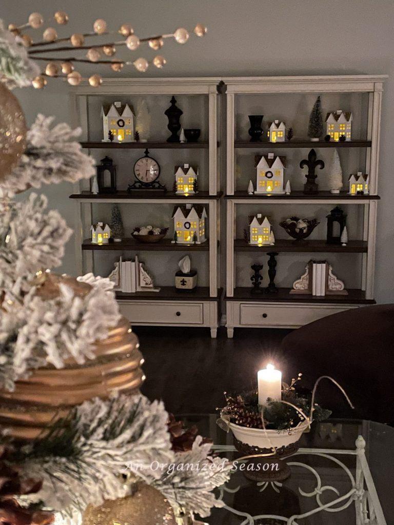 A twinkling Christmas village set up on a bookcase during the Tis the season nighttime home tour. 