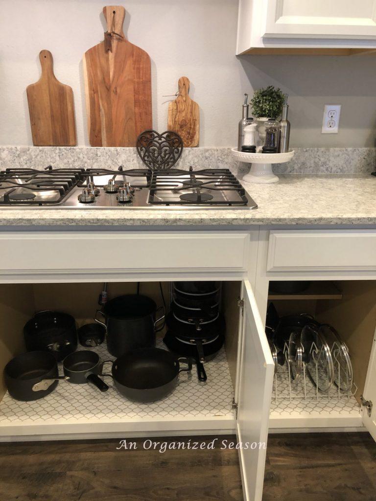 Two kitchen cabinets after home organization challenge with organized pots and lids. 