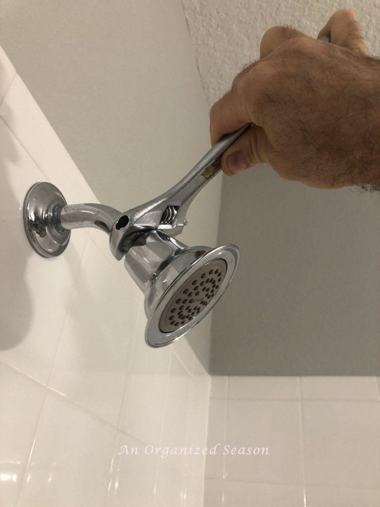 A man removing a shower head with a wrench, step one to easily install a new shower head