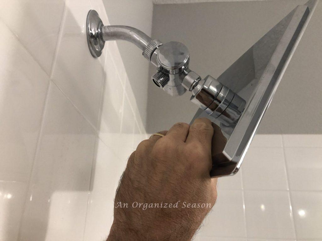 A man screwing a shower head onto a pipe showing a step to easily install a new shower head.